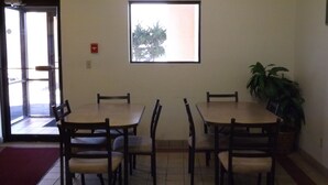 Un coin repas comprenant quatre tables et chaises en bois, une plante en pot et une fenêtre donnant sur des arbres.