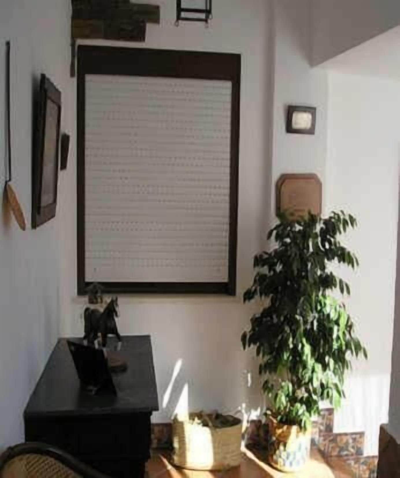 A room with a large framed document on the wall, a potted plant, and a small table with a decorative item.
