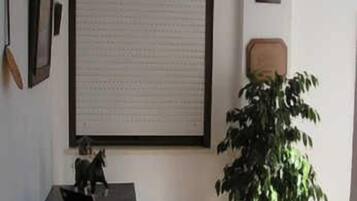 A room with a large framed document on the wall, a potted plant, and a small table with a decorative item.