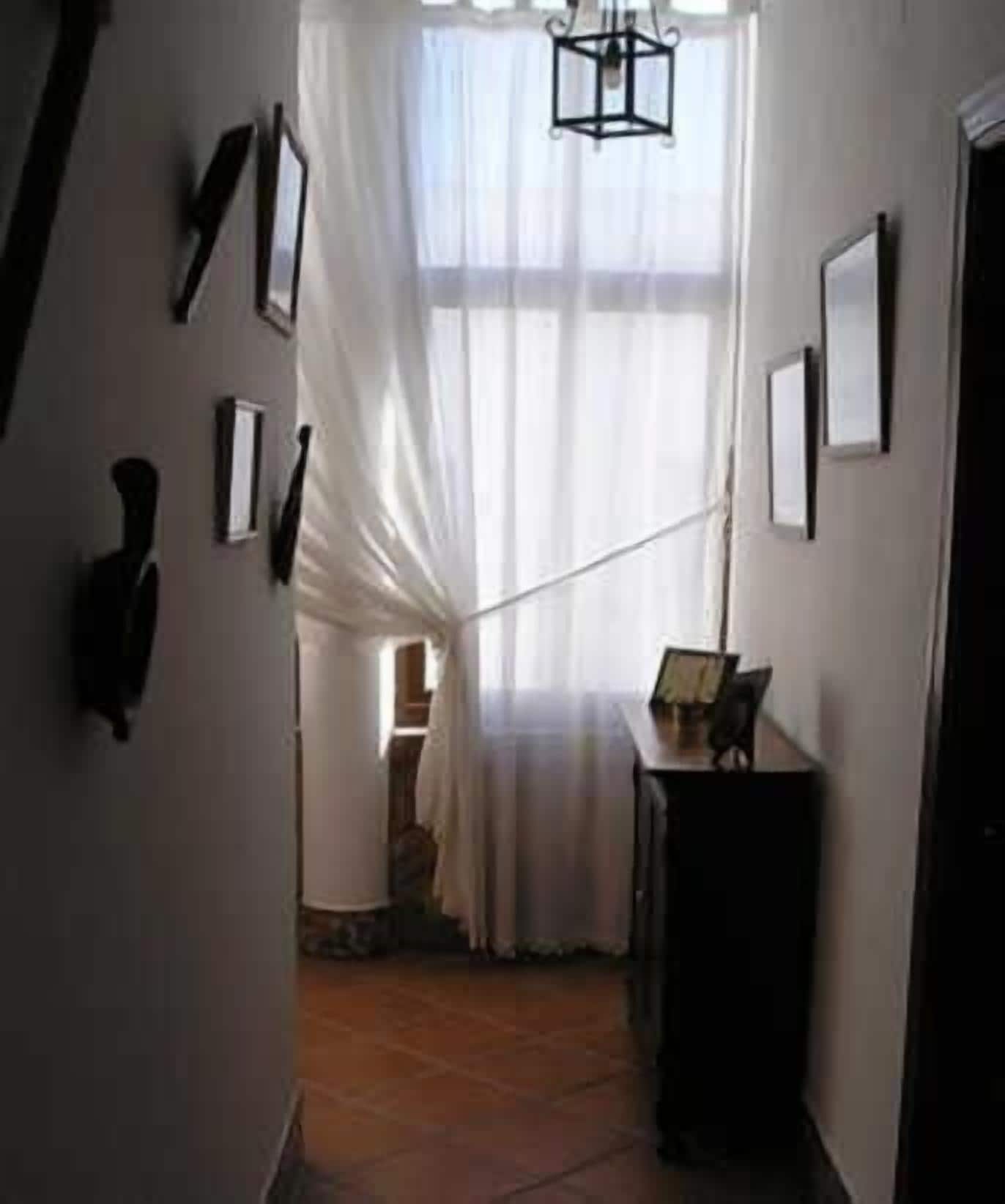 A narrow hallway with a staircase leading to a room with a large window and a table.