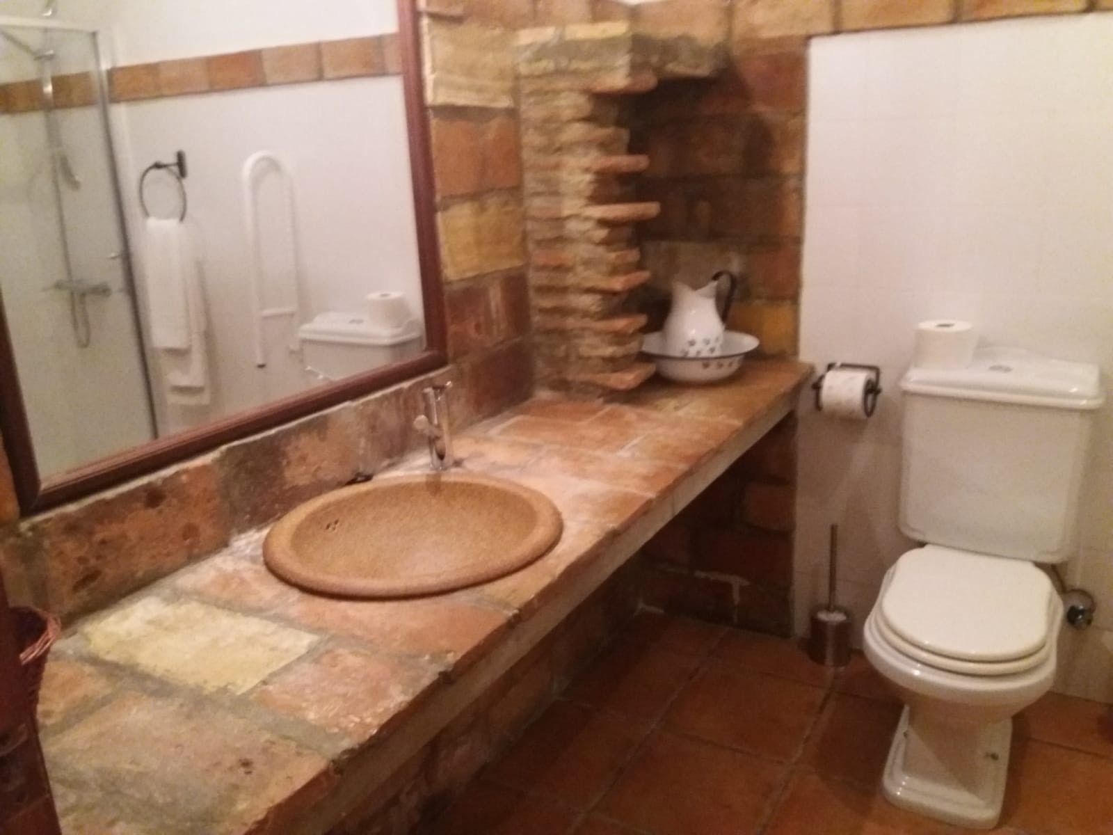 A bathroom with a stone sink, a toilet, and a mirror.