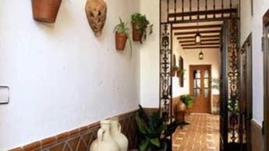 Un pasillo con baldosas de terracota, plantas en macetas y un banco de madera.