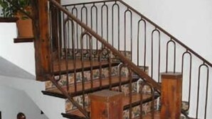 Una escalera de madera con barandillas de metal, una planta en maceta y un reloj fijado a la pared.