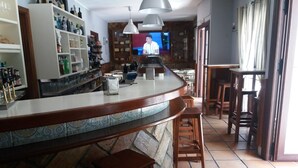 Zona de bar con piso de baldosas, taburetes de madera y una pantalla de televisión.