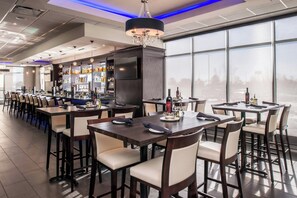 Zona de bar con diversas opciones de asientos, un televisor y un amplio ventanal con vistas al exterior.
