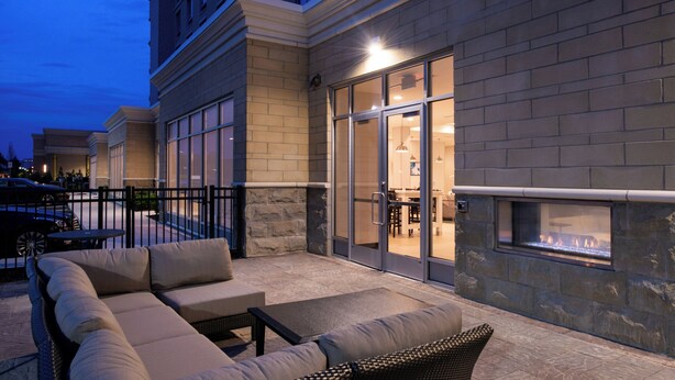 An outdoor seating area with a fire feature, a stone wall, and a glass door leading to an interior space.