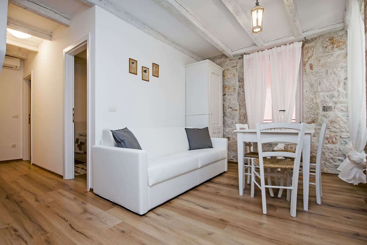 A white sofa with pillows, a dining table with chairs, and a stone wall.