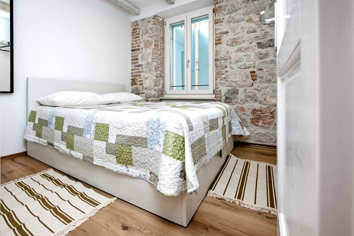 A bedroom with a bed, a window, and a stone wall.