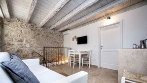 Una sala acogedora con una pared de piedra, un sofá blanco, una mesa de comedor con sillas y un televisor montado en la pared.