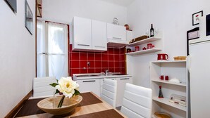 Una cocina compacta con armarios blancos, salpicadero de baldosas rojas y una zona de comedor con una mesa para dos.