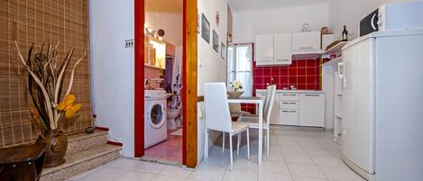 A compact kitchen with a washing machine, a dining area with a table and chairs, and a refrigerator.