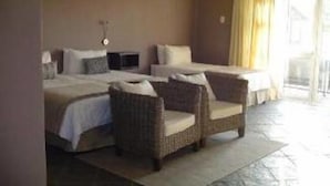 A hotel room with two beds, a wicker chair, and a large window with curtains. - Mount Lodge Humewood (Gqeberha (Port Elizabeth))