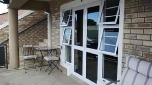 A patio area with a brick wall, a table with chairs, and a white-framed window. - Mount Lodge Humewood (Gqeberha (Port Elizabeth))