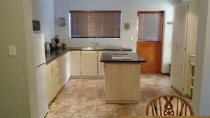 A compact kitchen with a central island, a sink, and cabinets. There is a window with blinds and a door with a window. - Lady Grey Walk Cottage (McGregor)