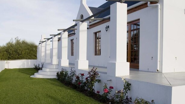 A modern white building with a flat roof, large windows, and a well-maintained lawn with flowers. - Lady Grey Walk Cottage (McGregor)