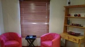 A room with two red armchairs, a small table, and a wooden shelf with decorative items. - Lady Grey Walk Cottage (McGregor)