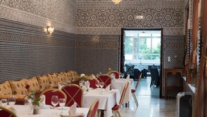 A dining area with patterned walls, tables set with white tablecloths, and red chairs.