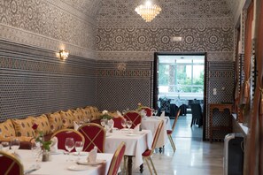 A dining area with patterned walls, tables set with white tablecloths, and red chairs.