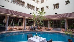 Un patio con piscina, mobiliario de exterior y un edificio de varios pisos y ventanas.