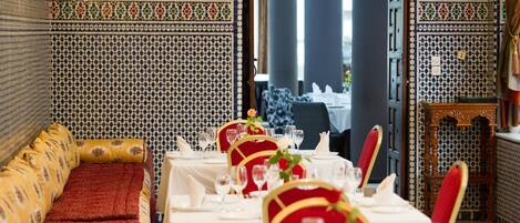 Un comedor con paredes estampadas, un sofá con cojines y una mesa con mantel blanco y sillas rojas.