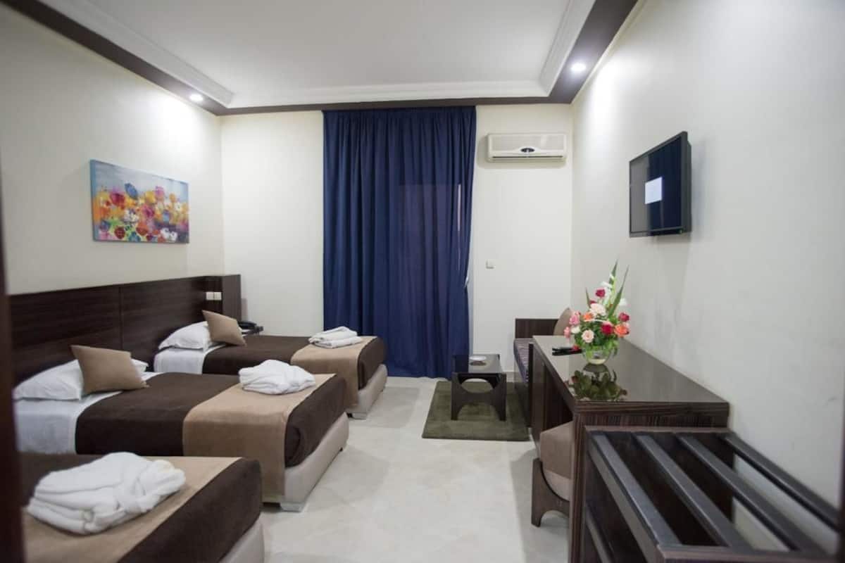 Ein Hotelzimmer mit zwei Betten, einem Schreibtisch, einem Sessel, einer Klimaanlage, einem Fernseher und einem Bild an der Wand.