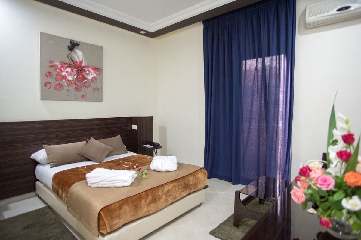 A hotel room with a bed, a nightstand, a telephone, a wall-mounted air conditioner, and a painting.