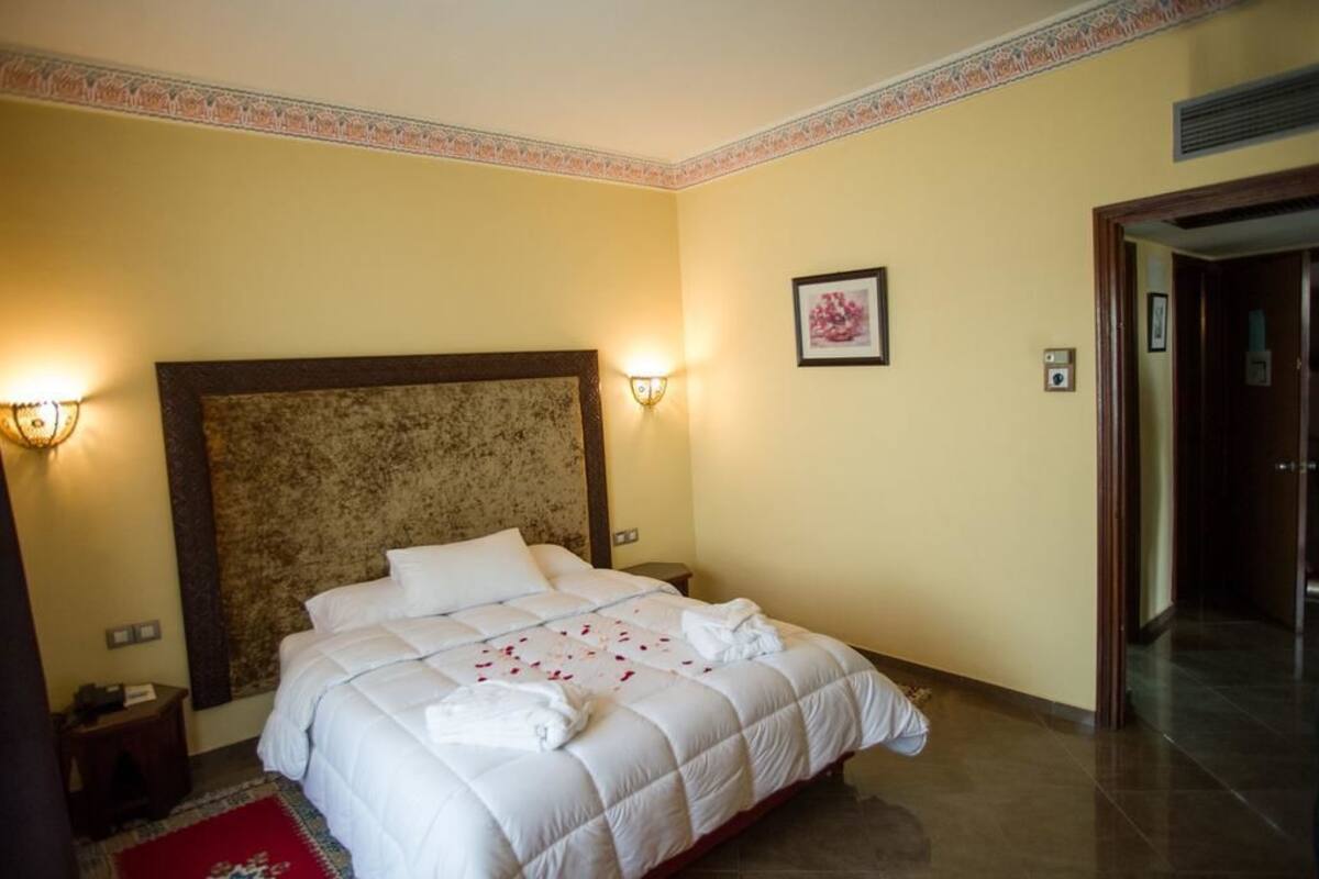 Ein Hotelzimmer mit einem großen Bett, zwei Nachttischlampen, einem gerahmten Bild an der Wand und einem roten Teppich.
