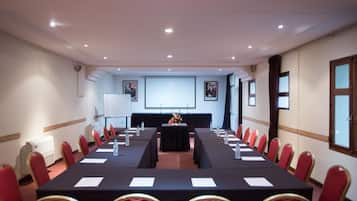 Une salle de conférence avec une longue table, des chaises rouges, un écran de projection et un tableau blanc.