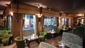 Un restaurante con sillas y mesas tapizadas de verde, ventanas amplias con cortinas, y vistas al exterior.