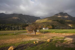A rural landscape with a farmhouse, rolling hills, and a cloudy sky. - Mont Angelis Retreat (Stellenbosch)