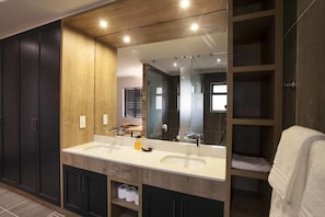 A modern bathroom with a double sink, dark cabinets, a wooden accent wall, and a large mirror.