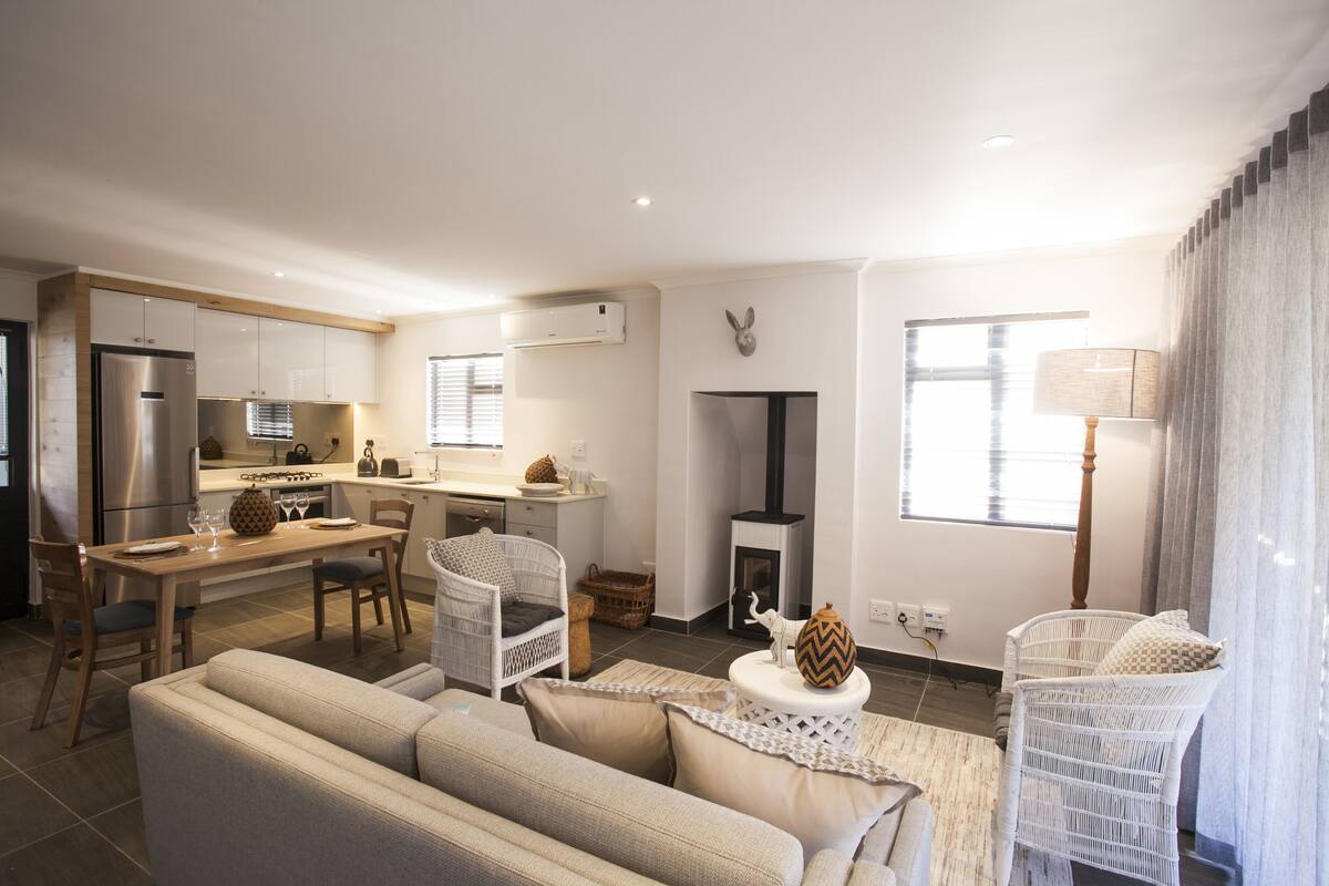 A modern kitchen with a dining area, a fireplace, and a living room with a sofa and chairs.