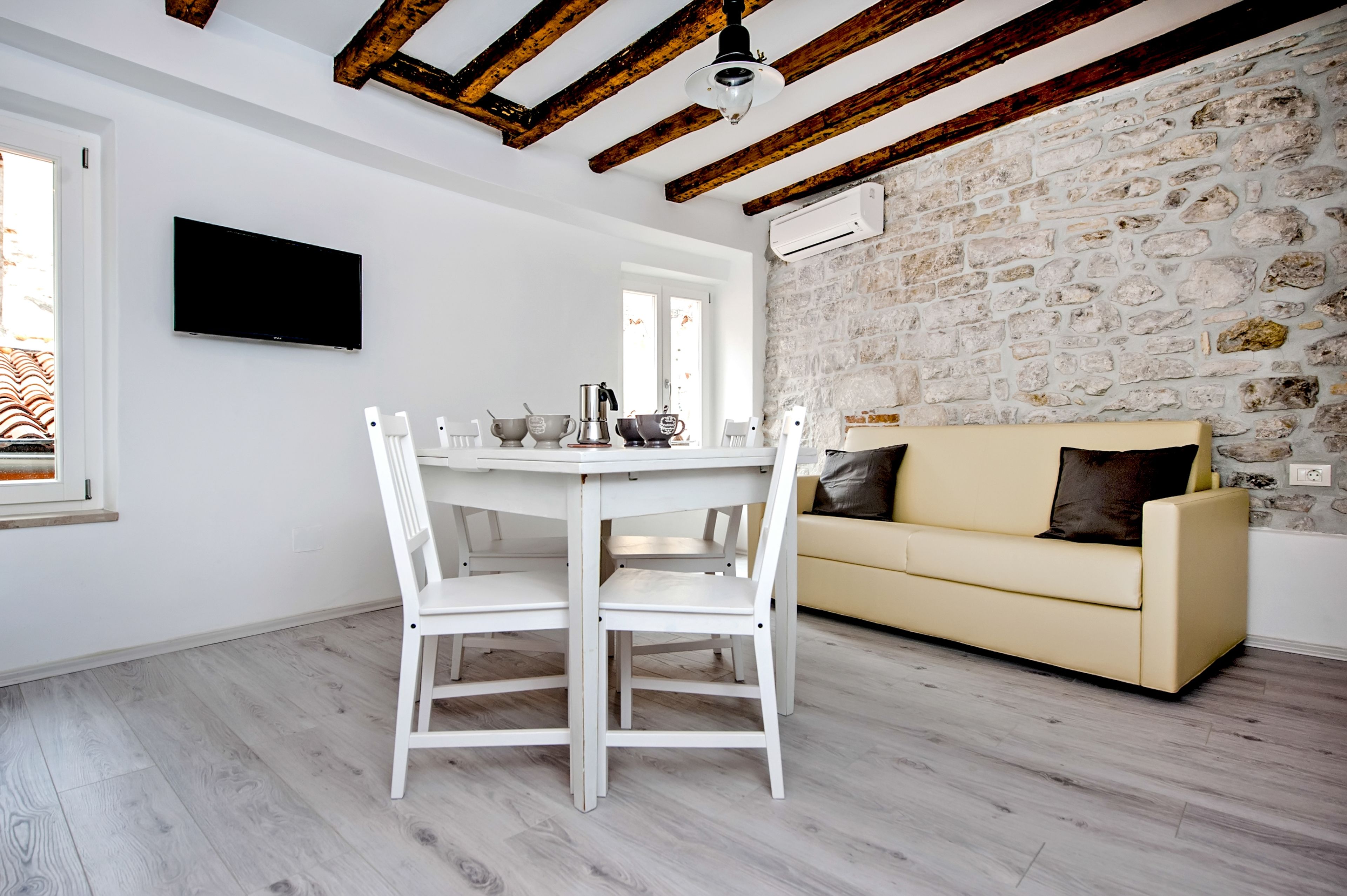 A modern living room with a stone wall, a white sofa, a dining table with chairs, and a mounted TV.