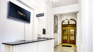 Un comptoir d’accueil doté d’un téléviseur à écran plat affichant le logo de « Matisse Apartments & Suites », une enseigne indiquant la réception et une œuvre d’art encadrée accrochée au mur.