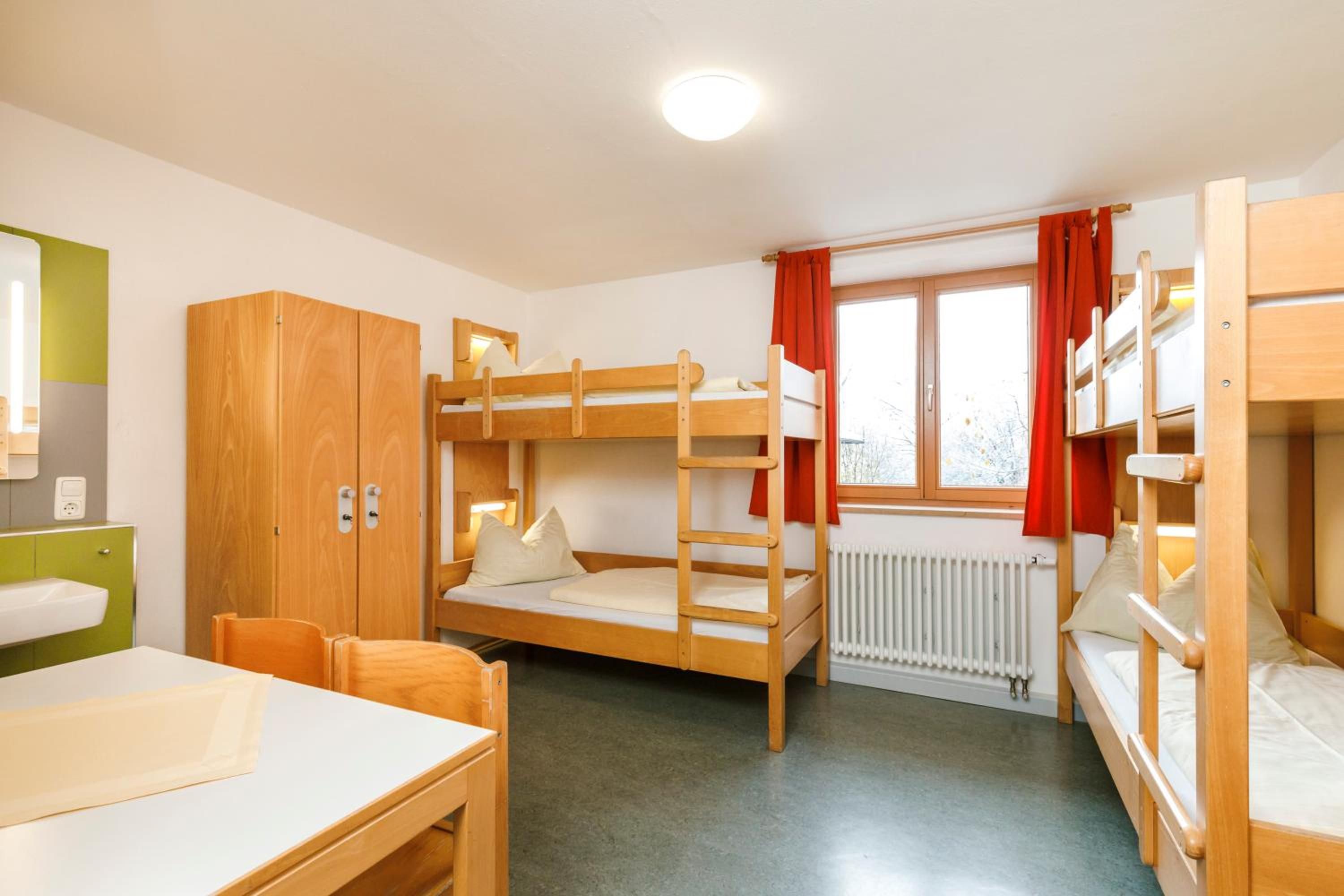 Une chambre de dortoir avec des lits superposés, un bureau, une chaise, une armoire et une fenêtre avec des rideaux.