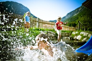 Un enfant joue dans l’eau près d’un toboggan, entouré d’une clôture en bois et de verdure.