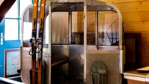 Une cabine de télésiège avec une structure extérieure en métal et des fenêtres en verre, des parois en bois et une rambarde en métal au premier plan.