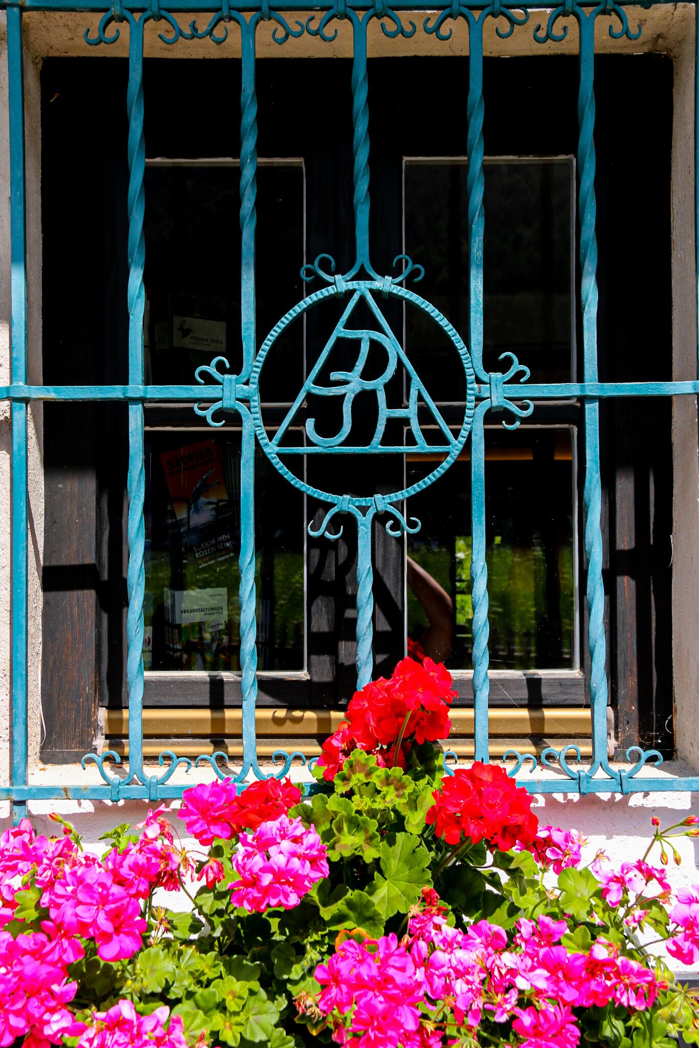 A window with a decorative metal grille and a logo, surrounded by vibrant pink flowers.