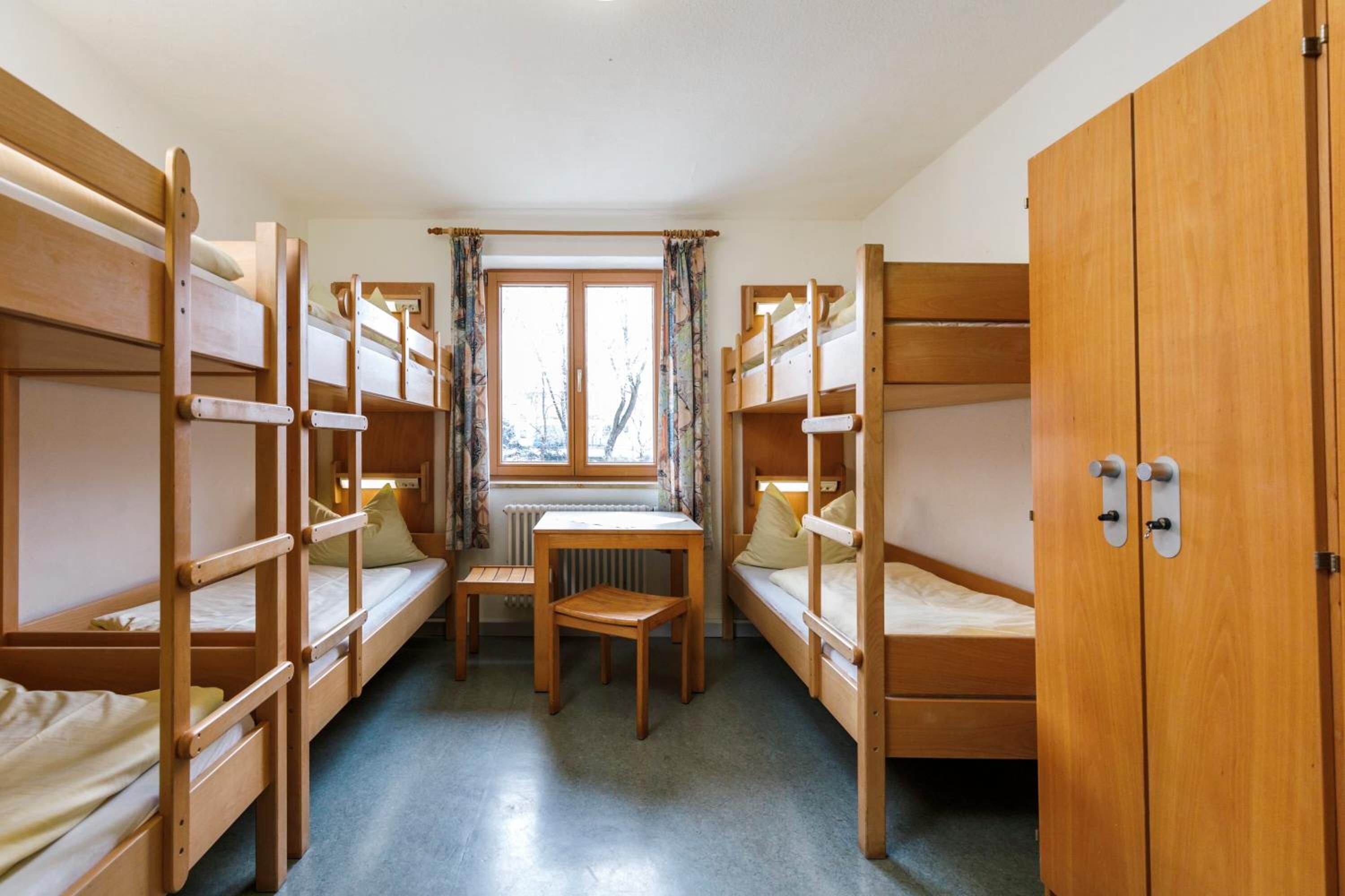 Ein Schlafsaalzimmer mit Etagenbetten, einem kleinen Tisch und einem Fenster mit Vorhängen.