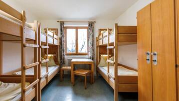 Ein Schlafsaalzimmer mit Etagenbetten, einem kleinen Tisch und einem Fenster mit Vorhängen.