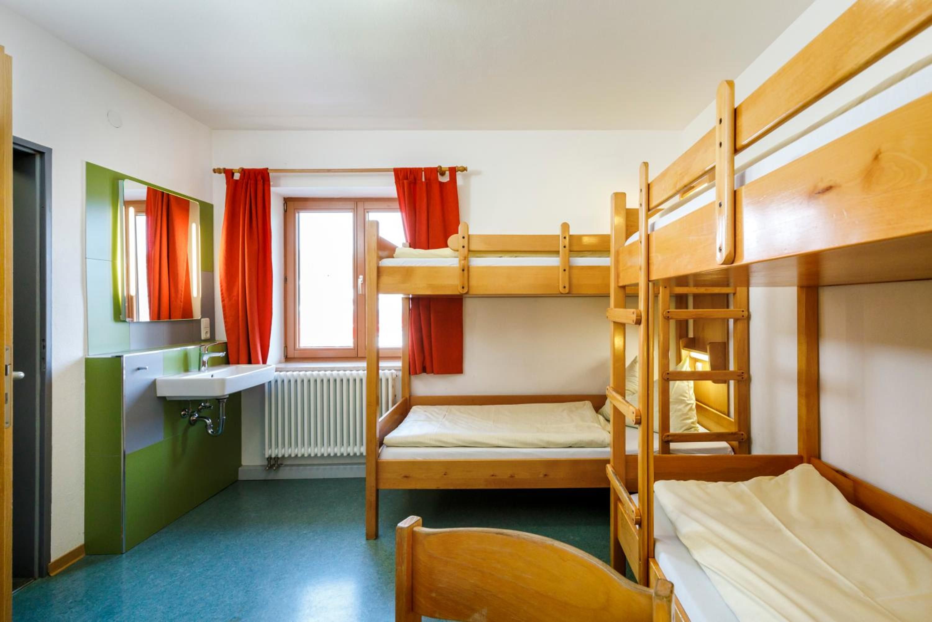 Ein Schlafsaalzimmer mit Etagenbetten, einem Waschbecken, einem Spiegel und einem Fenster mit Vorhängen.