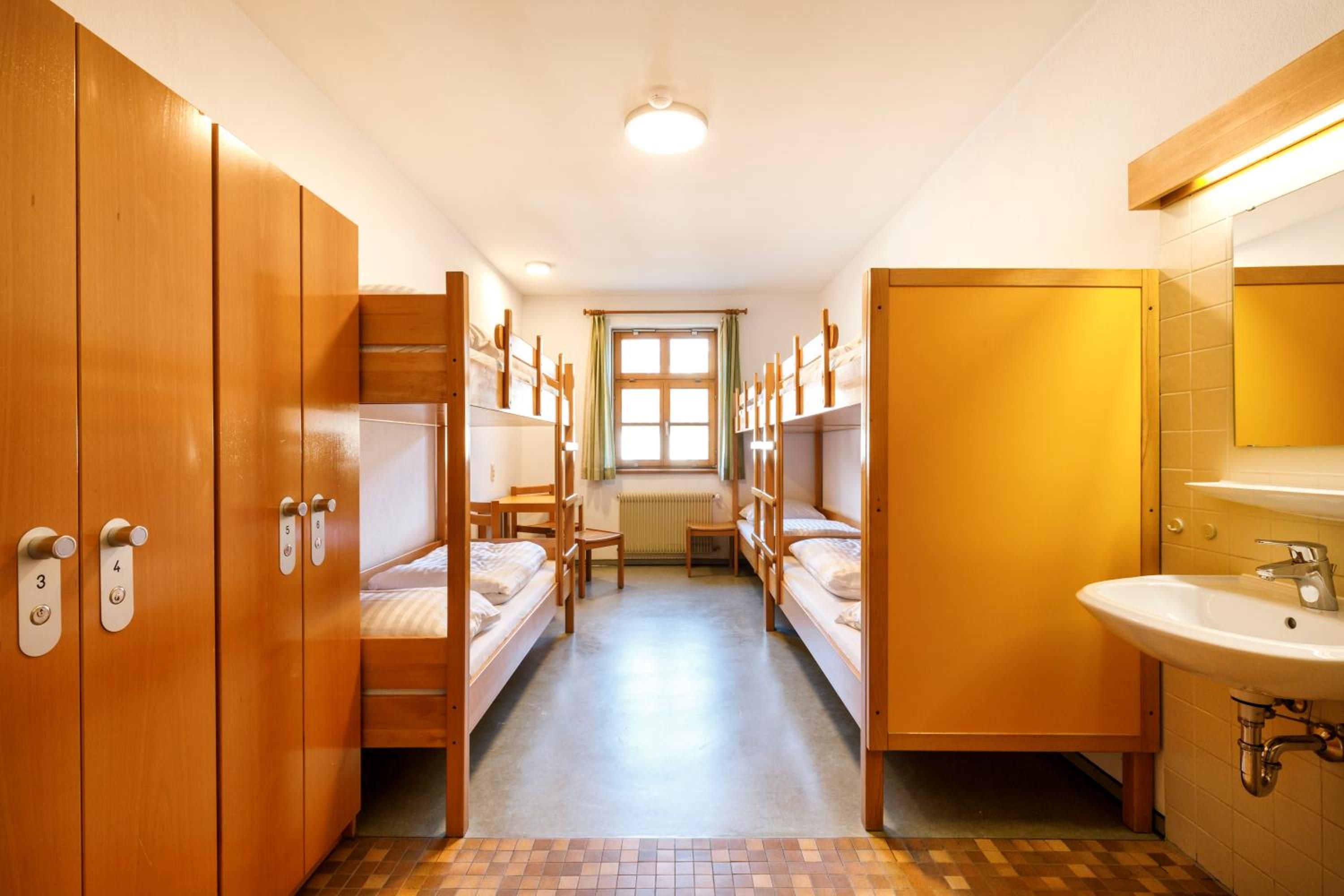 Un dormitorio con literas, una ventana, un radiador y un baño con lavamanos y espejo.
