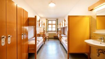 Un dormitorio con literas, una ventana, un radiador y un baño con lavamanos y espejo.