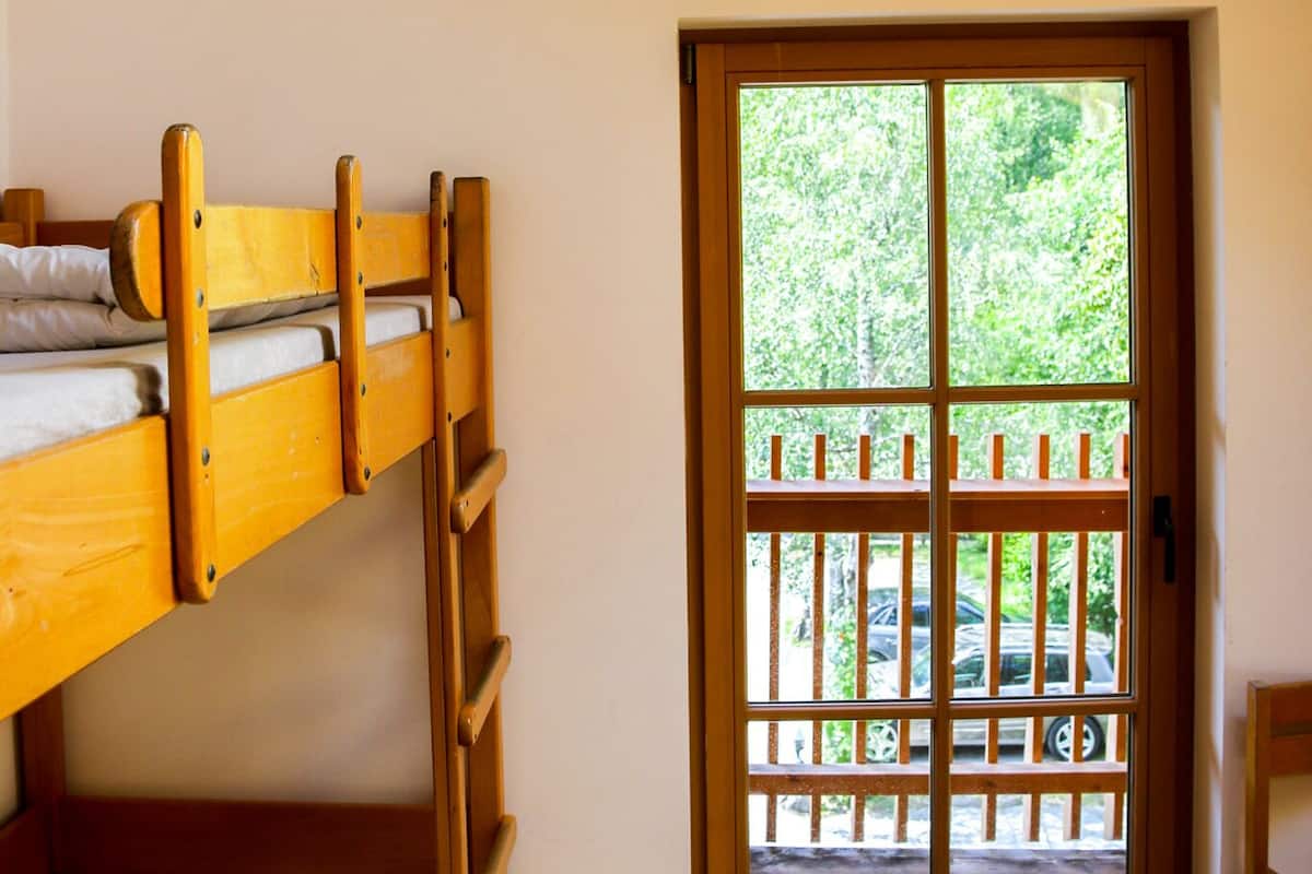 Een stapelbed in een kamer met een houten plafond en een deur naar een terras.