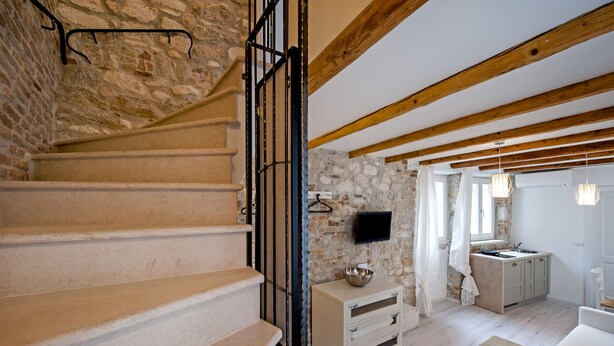 A staircase with stone walls, a kitchen area with a sink and cabinets, and a living space with a sofa and a television. - Apartment and Studio CA 3 VIE (Rovinj)
