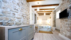 A compact room with a stone wall, wooden beams, a bed, a TV, and a kitchenette. - Apartment and Studio CA 3 VIE (Rovinj)