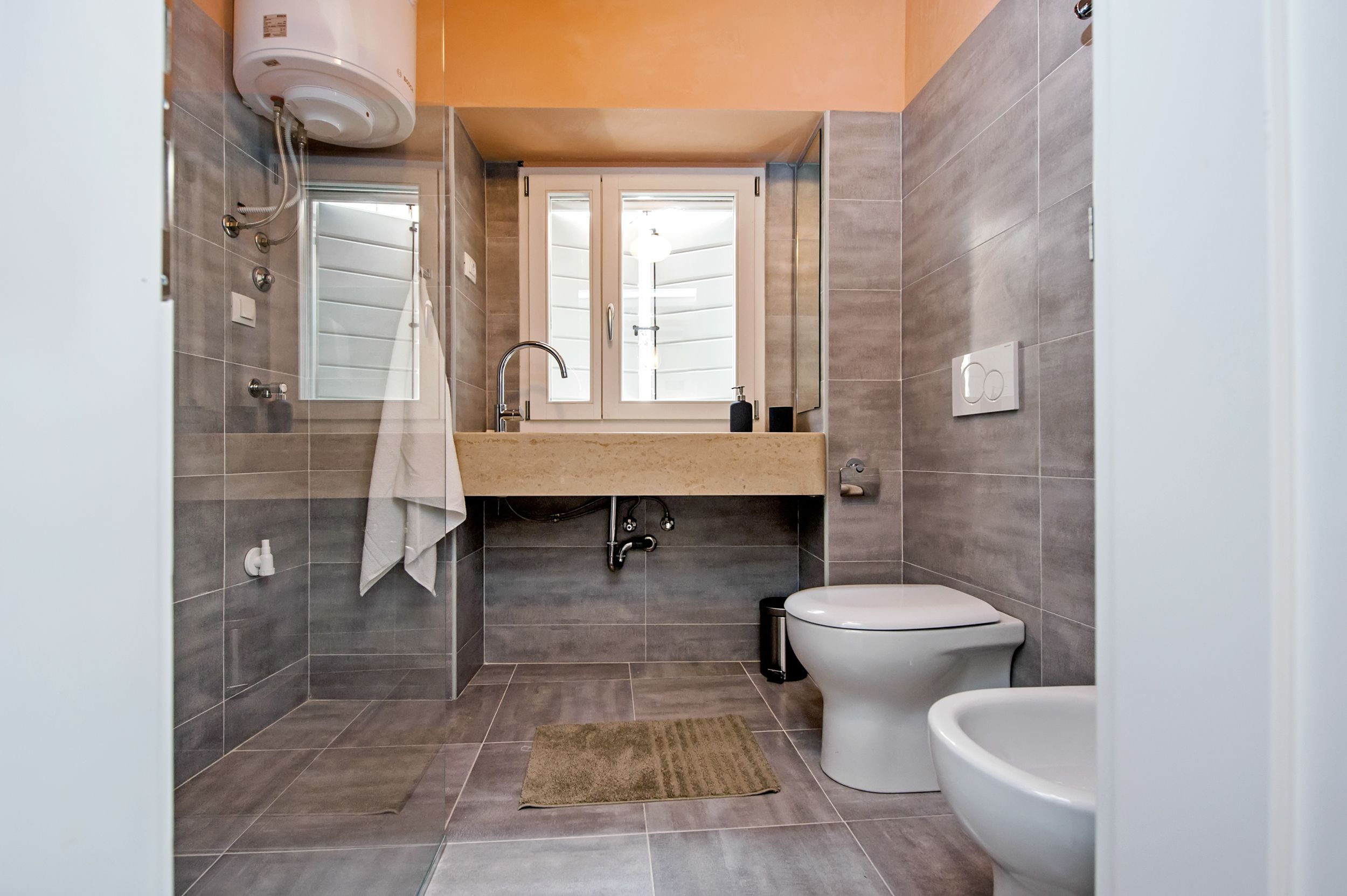 A modern bathroom with a glass shower enclosure, a sink with a mirror, a toilet, and a bidet.