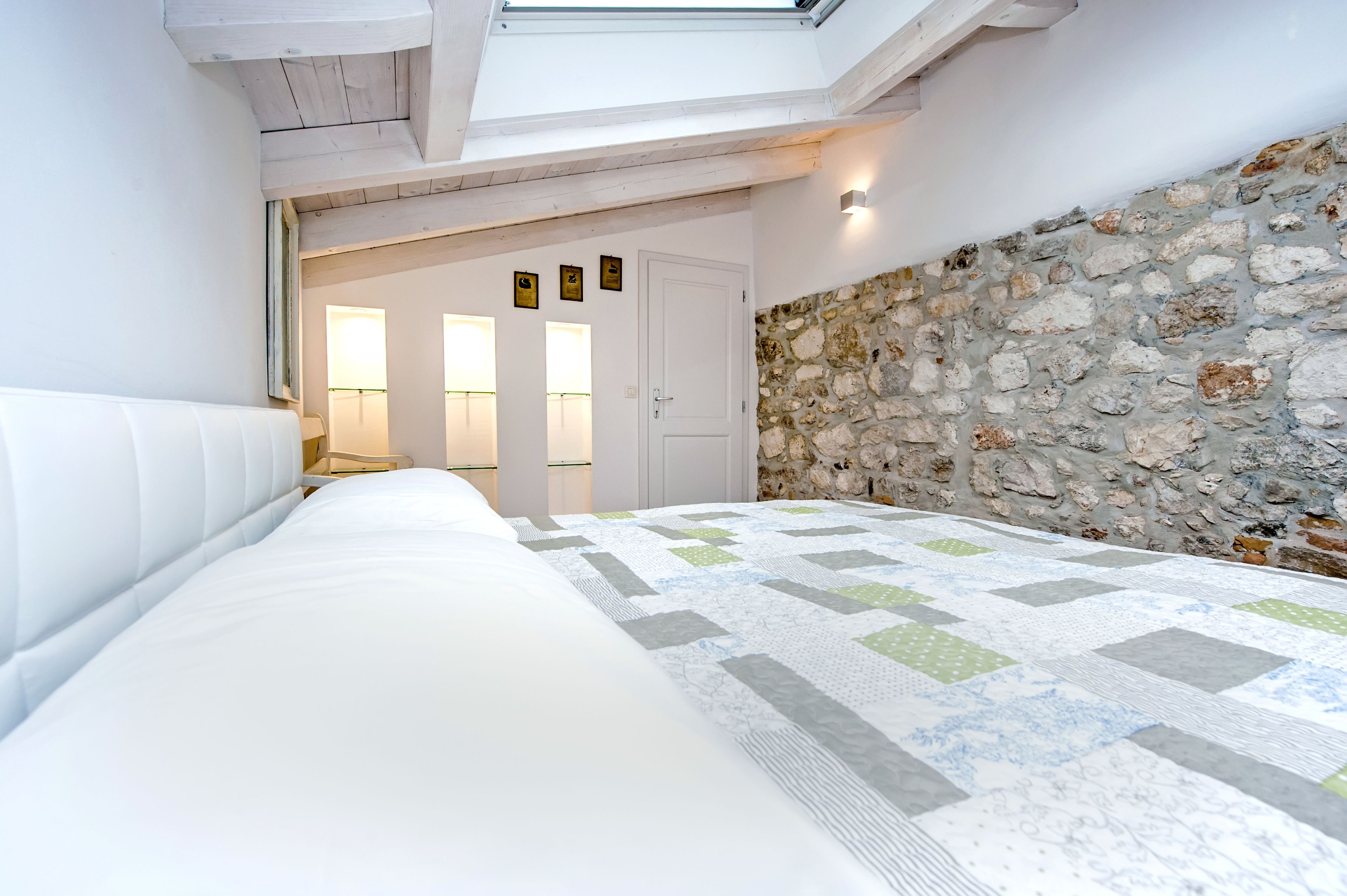 A bedroom with a skylight, a stone wall, and a bed with a quilt.