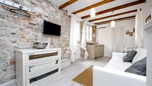 A modern living room with a stone wall, wooden beams, a white sofa, and a kitchen area in the background. - Apartment and Studio CA 3 VIE (Rovinj)