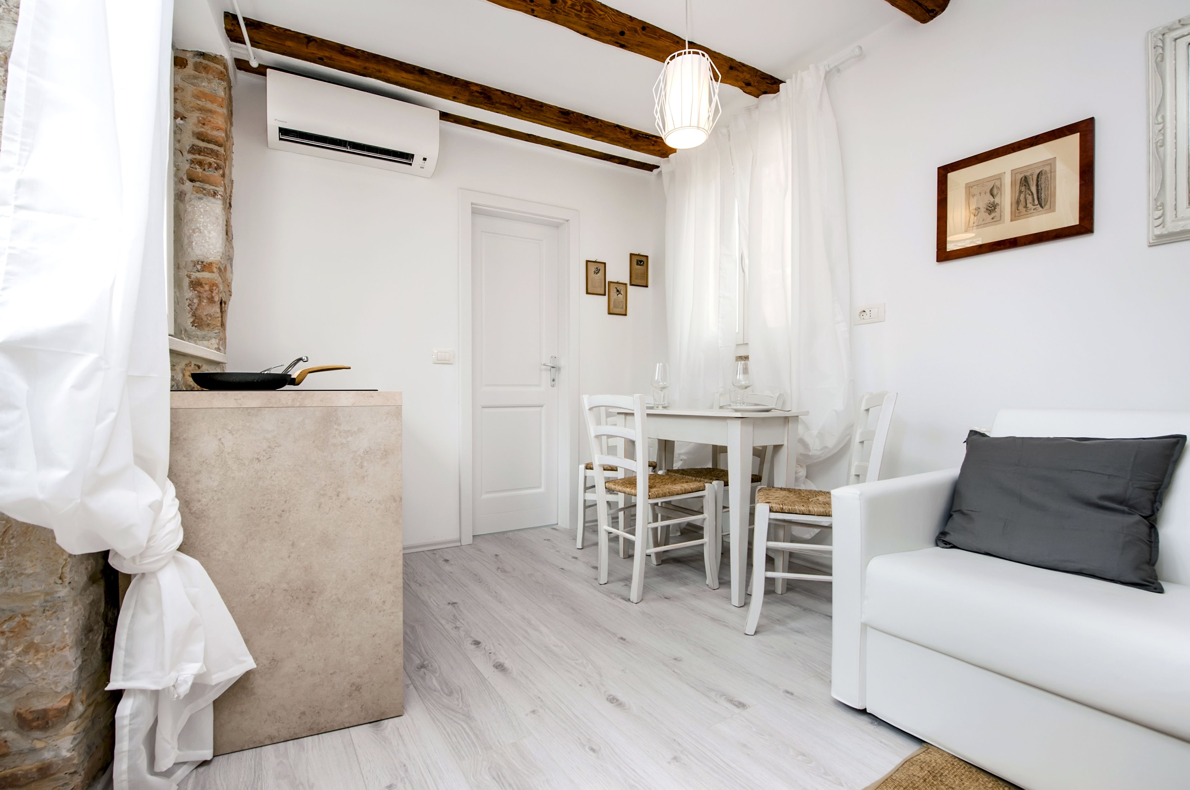 A room with a white sofa, a dining table with chairs, a kitchen area with a stove and utensils, and a white door.